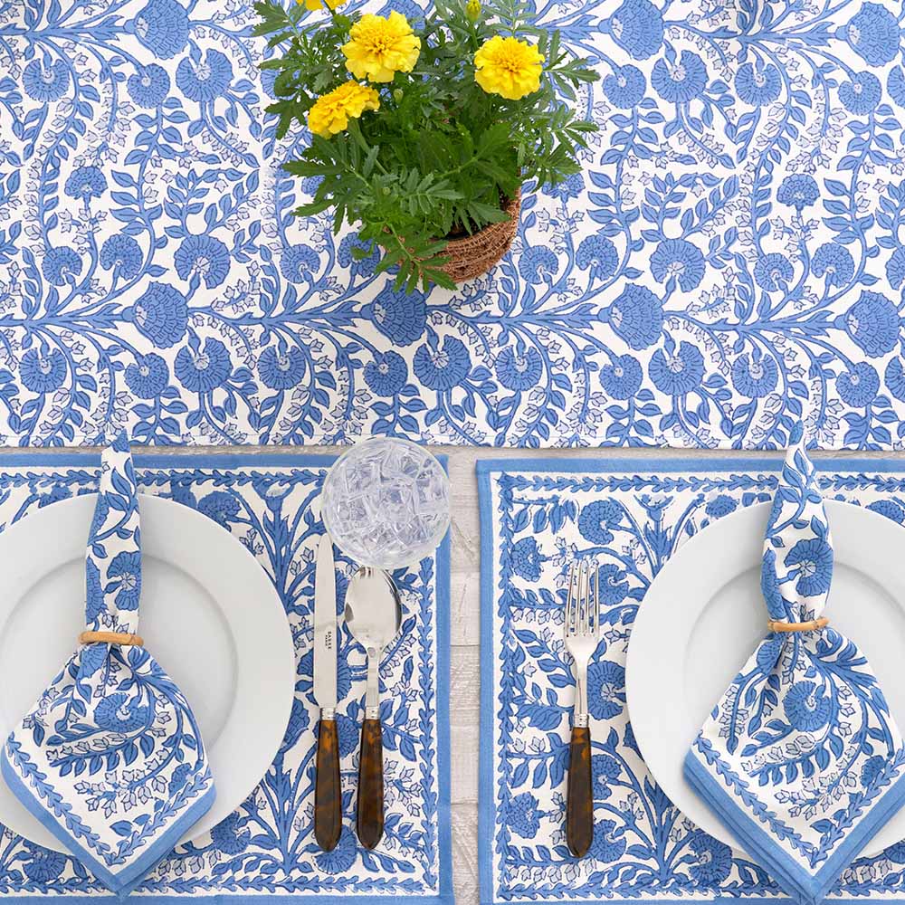 Table setting with blue floral tablecloth, white plates, and silverware on a white background.