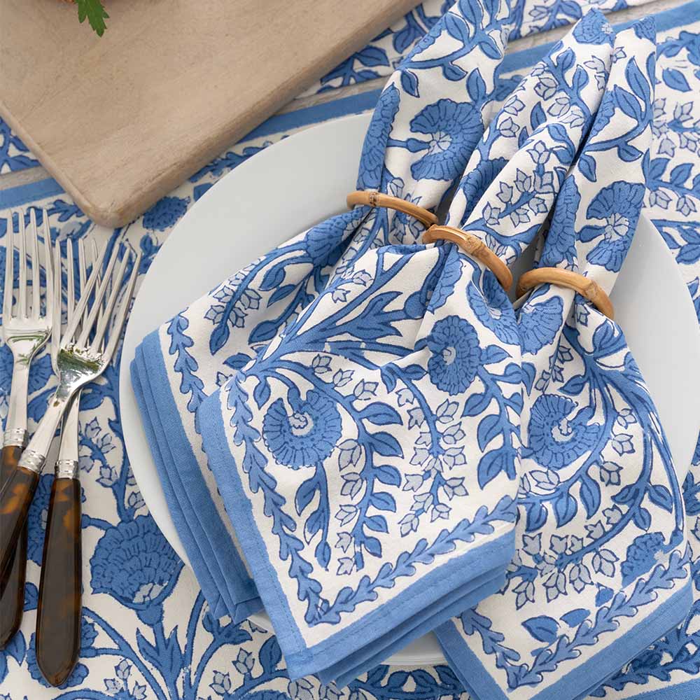 Blue and white floral-patterned napkin on a table with cutlery and plates.