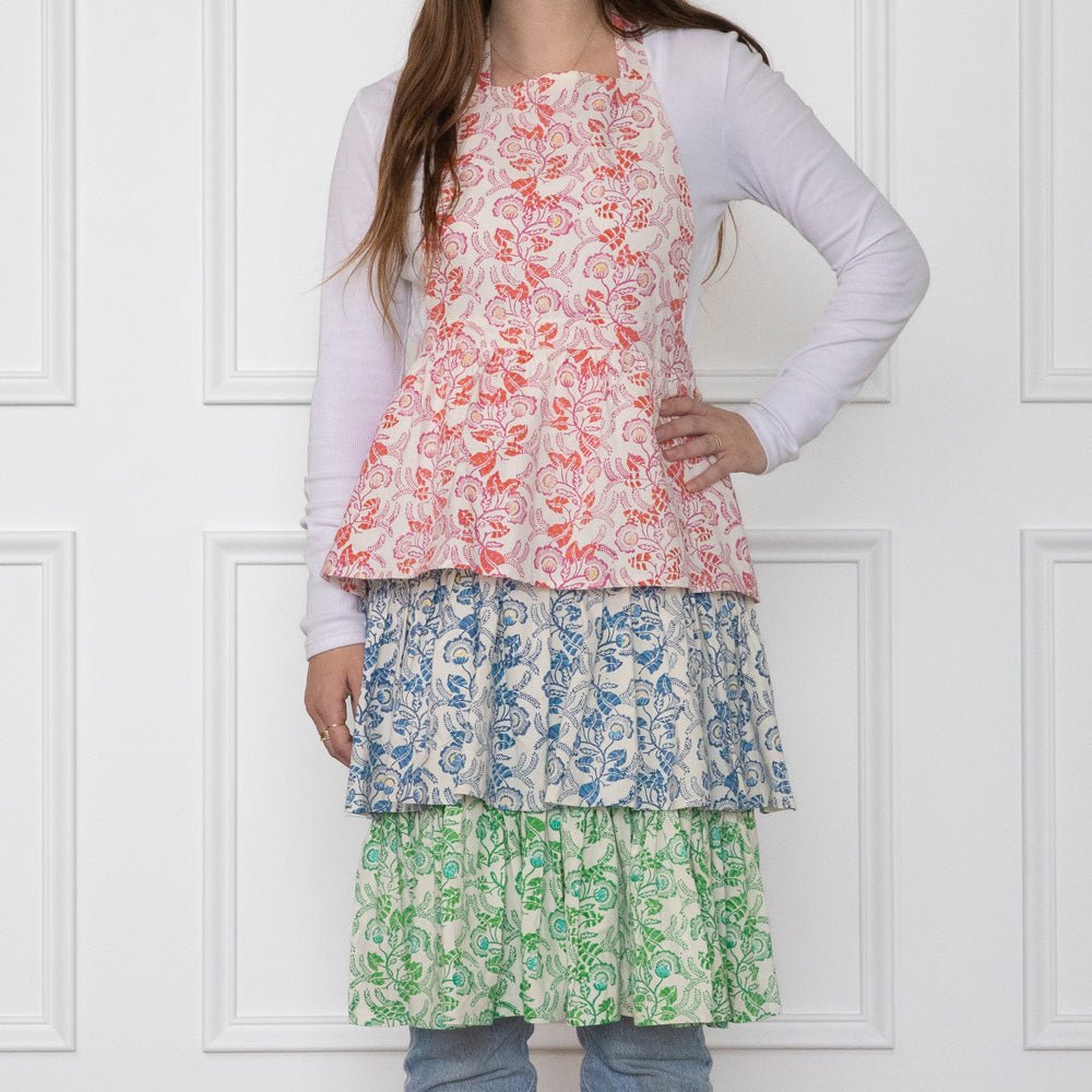 A person wearing a multicolored floral apron with ruffled tiers in blue, pink, and green, standing against a white background.
