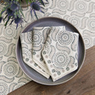 A set of folded cloth napkins with a geometric pattern, displayed on a table with other tableware.
