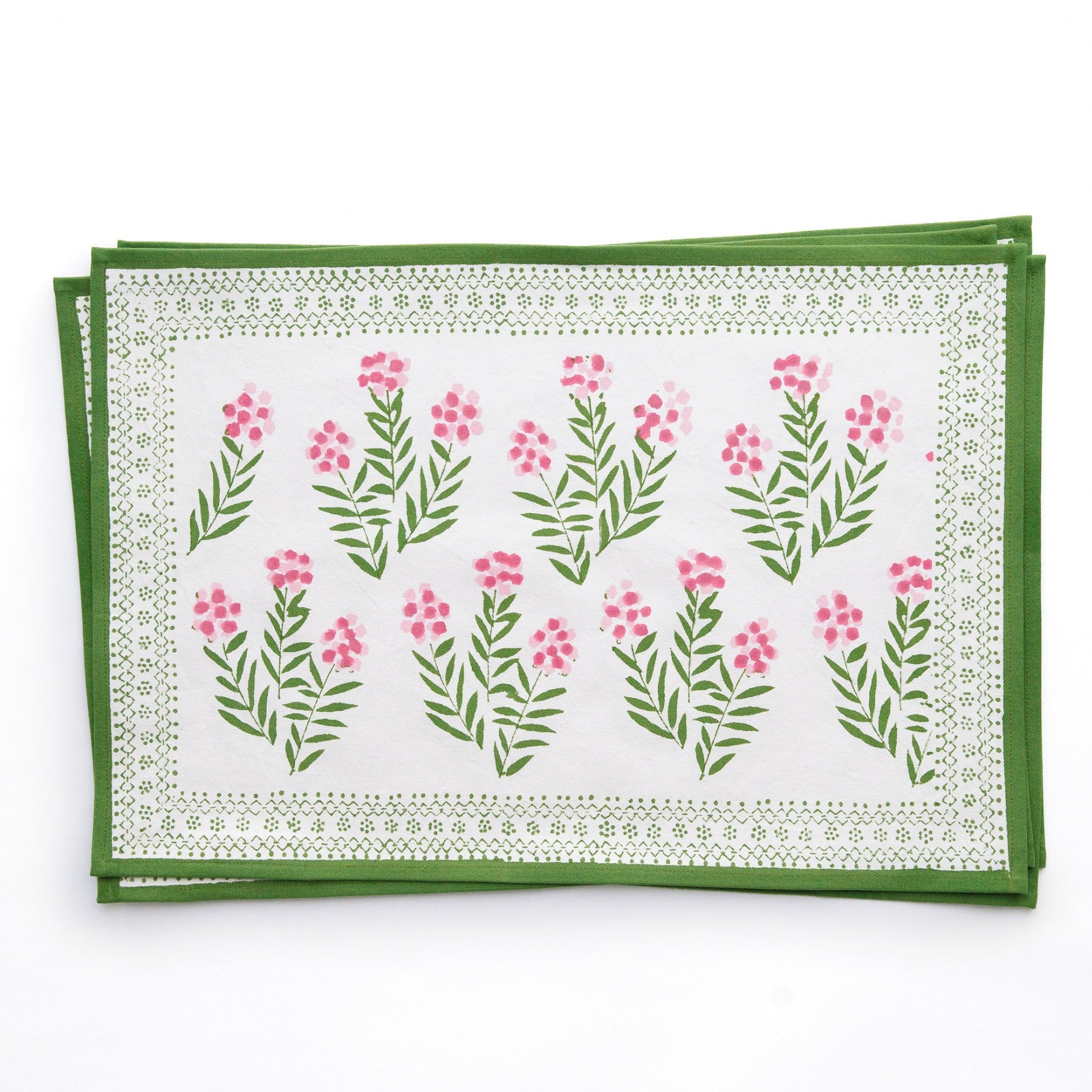 A set of four placemats with a floral pattern, featuring pink flowers and green leaves on a white background, placed on a white surface.