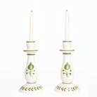 Pair of white candlesticks with green decorative patterns on a white background