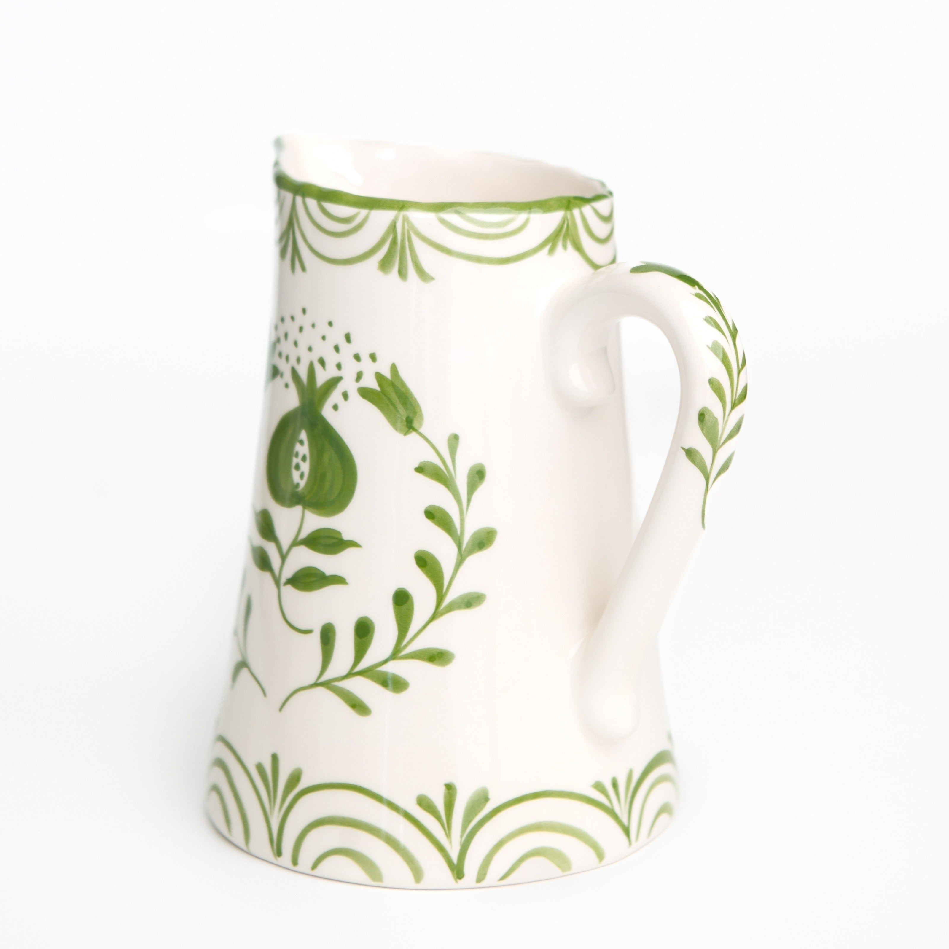 White ceramic pitcher with green leaf and pomegranate pattern on a white background