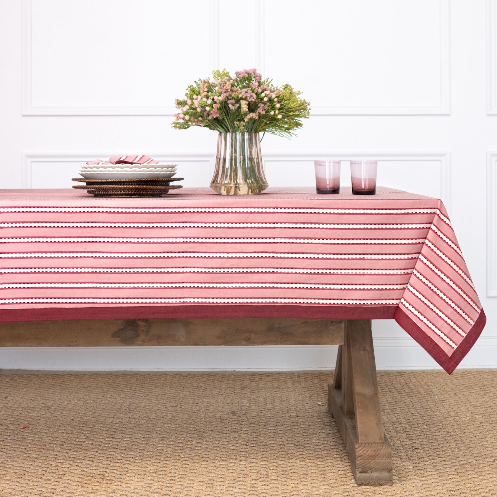 Table with a red and white striped tablecloth, flowers, and candles in a room.