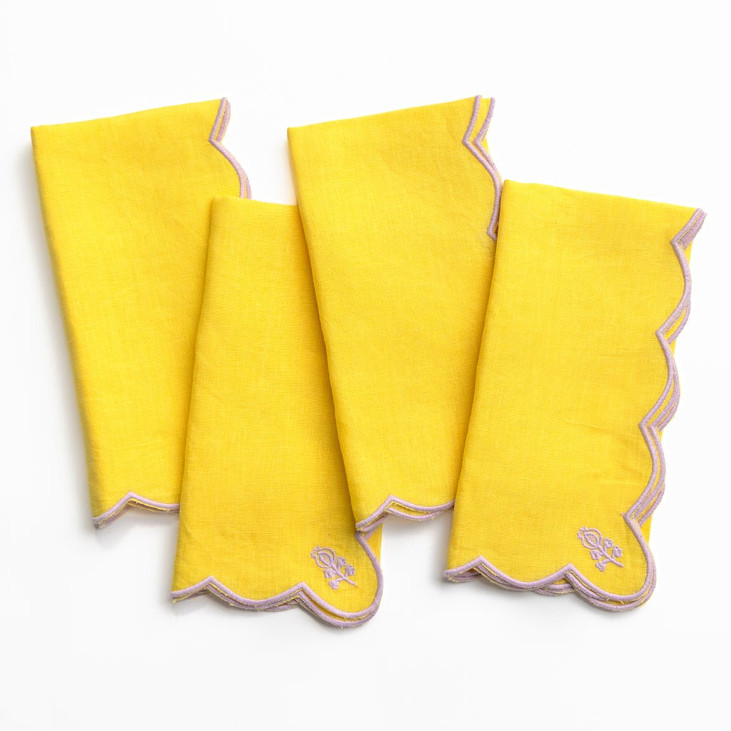 Four yellow napkins with pink scalloped edges on a white background