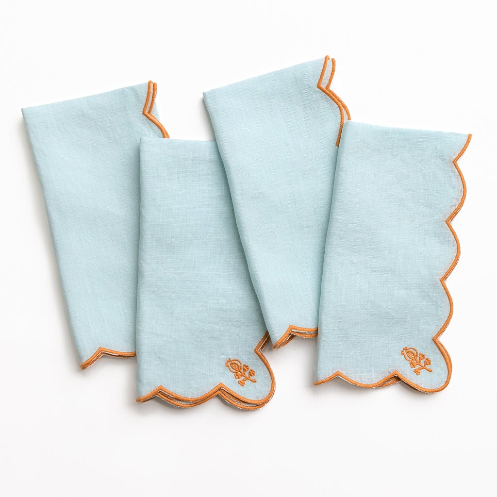 Set of four light blue napkins with orange trim on a white background