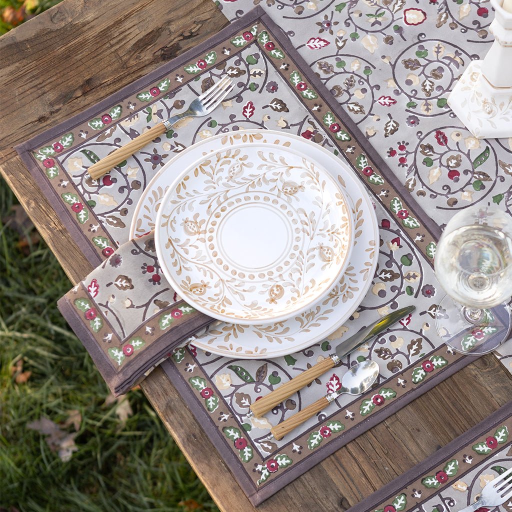 Set table with decorative plates, cutlery, and placemats on a wooden table outdoors.