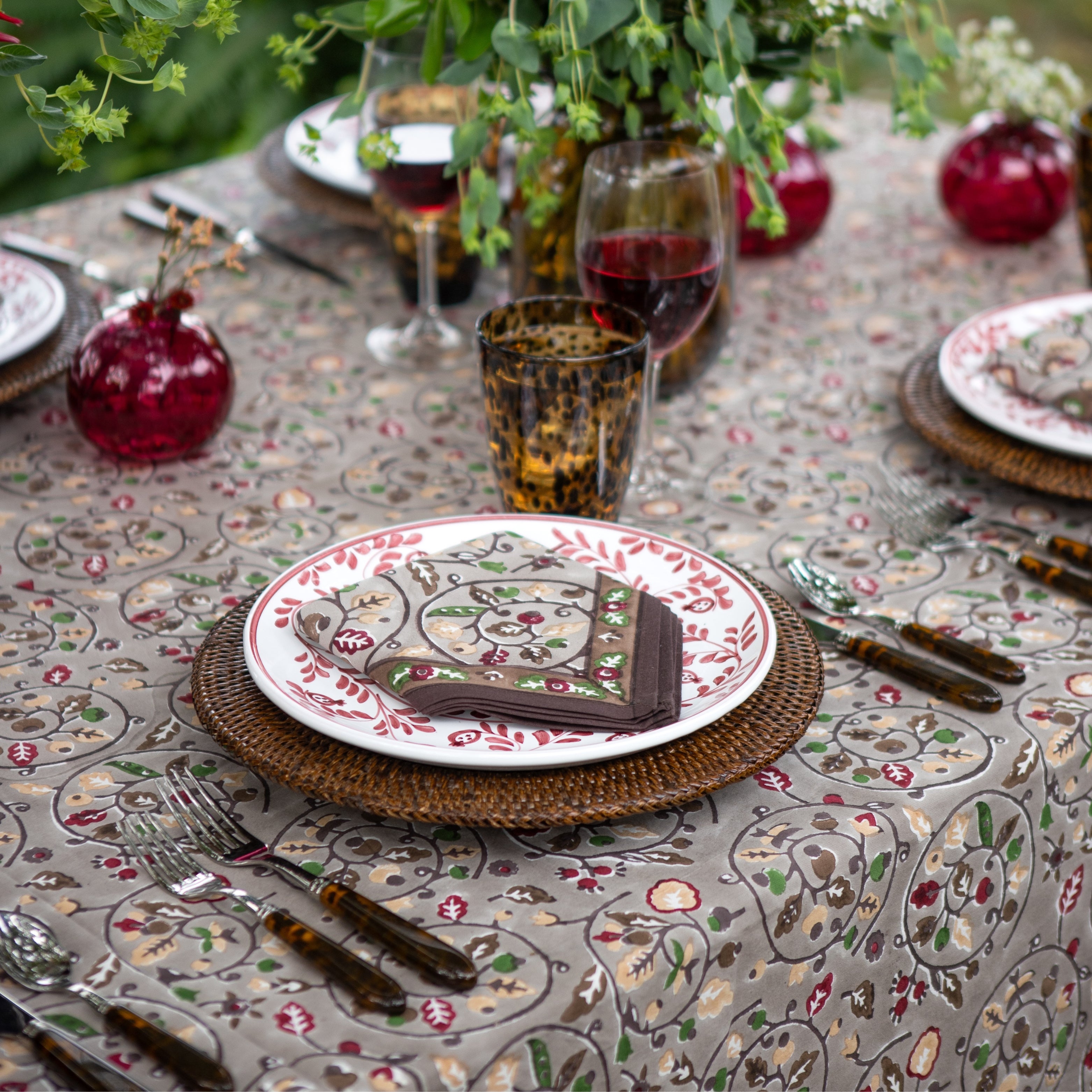 Elegant table setting with floral-patterned tablecloth, plates, and cutlery.