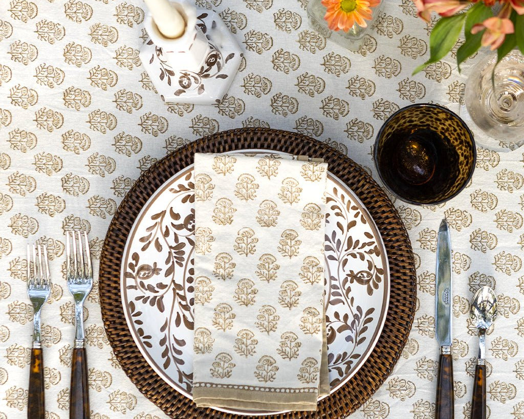 folded beige and white indian print napkin on a plate sitting on a tablecloth