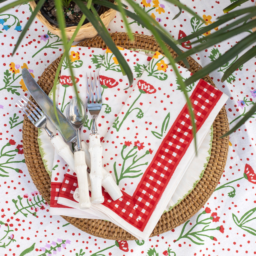 Colorful floral napkins stacked on ceramic plate with plant peaking in corner.