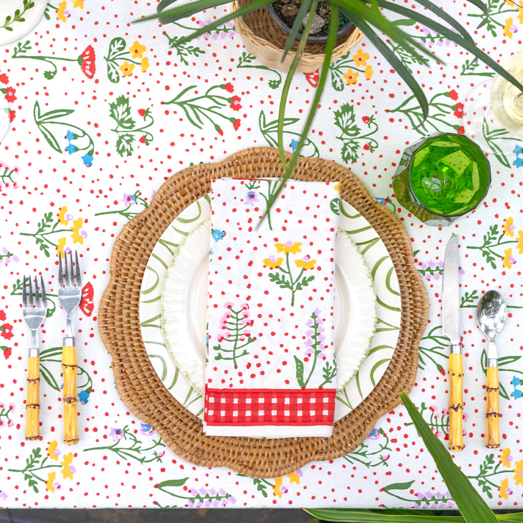 Dining table setting with a patterned tablecloth, woven charger, and colorful cutlery.