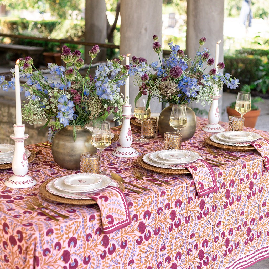 Decorative table setting with floral centerpieces, candles, and patterned tablecloth outdoors.