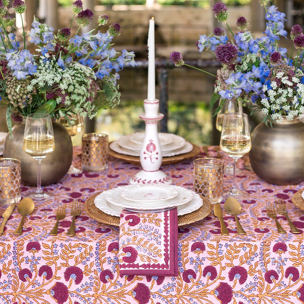 Elegant dining table setting with floral centerpieces, candles, and patterned tablecloth.