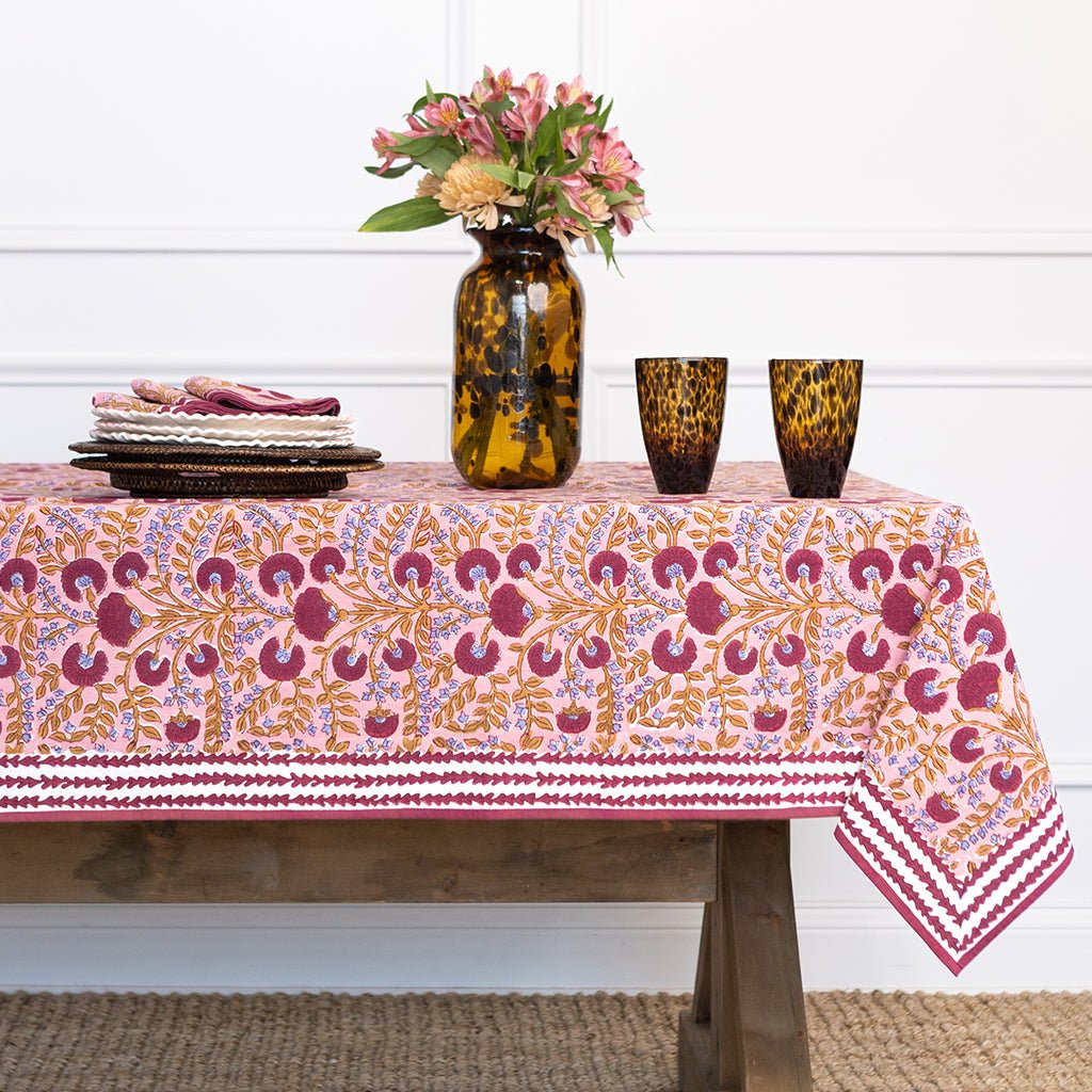Table with a patterned tablecloth, vase with flowers, and glasses on a white wall background