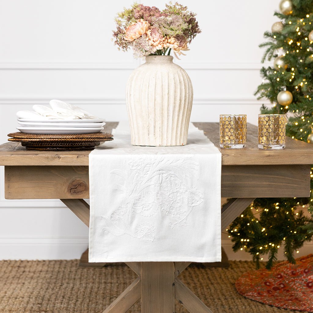 Decorative table setting with a vase, candles, and a Christmas tree in the background.