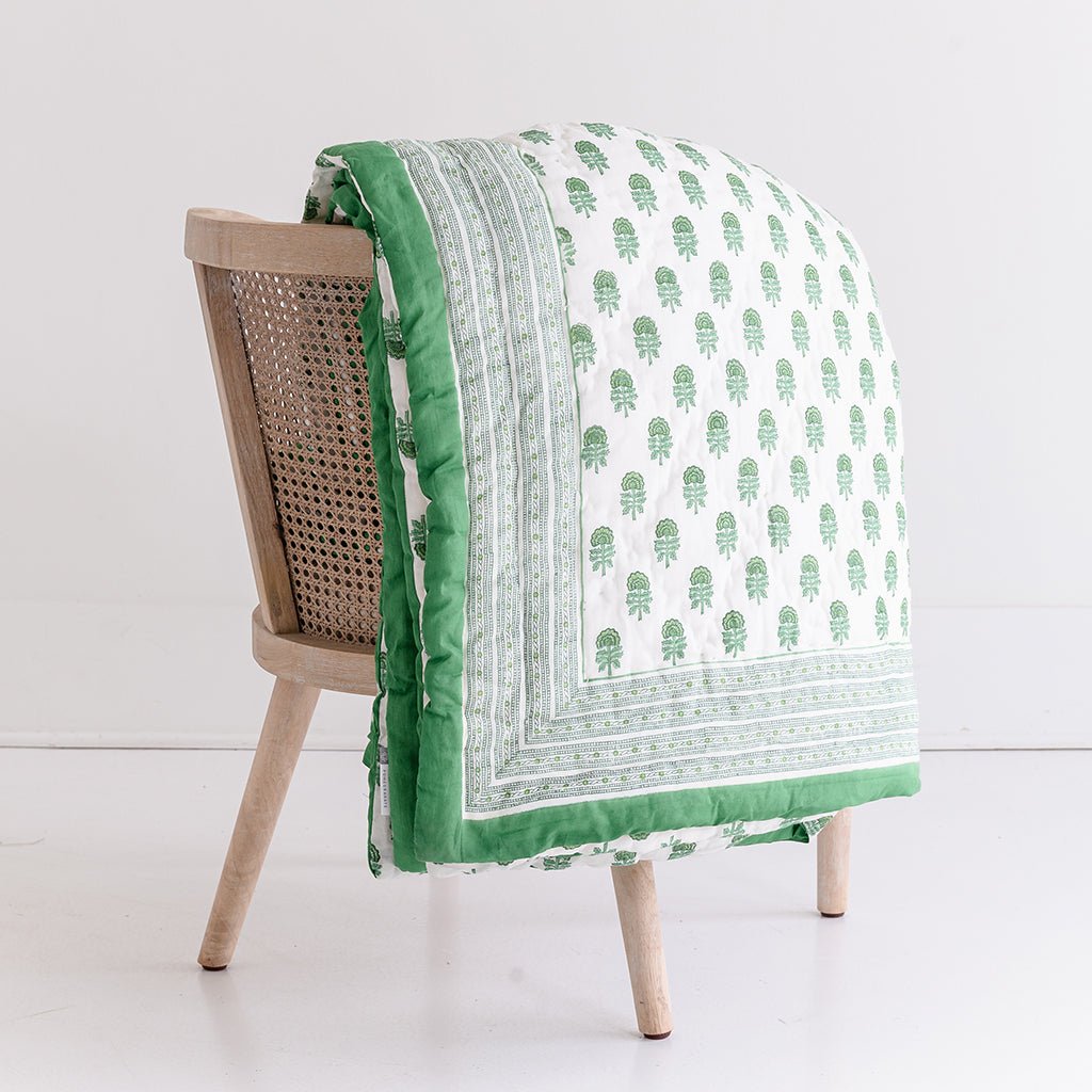 Green and white patterned quilt draped over a wooden chair on a white background
