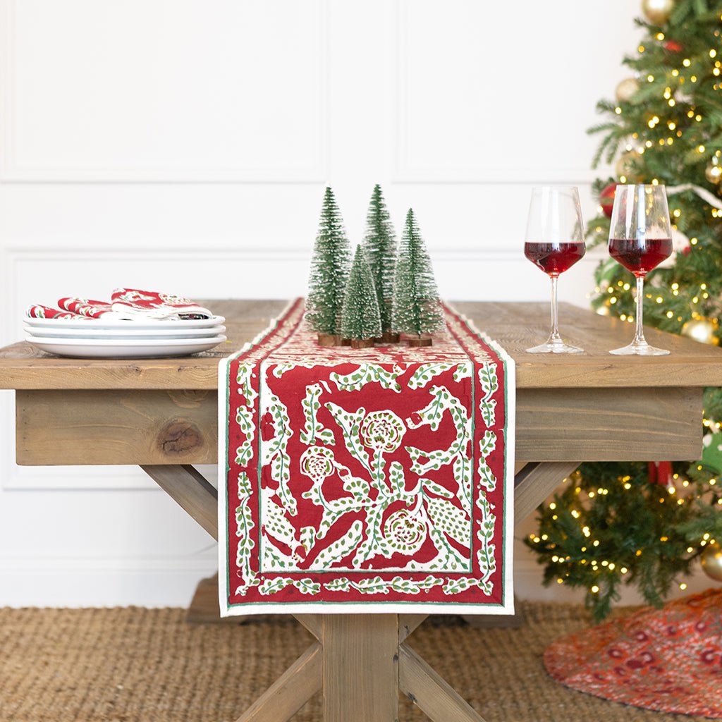 Dining table set with a red and white patterned table runner, wine glasses, and Christmas decorations.