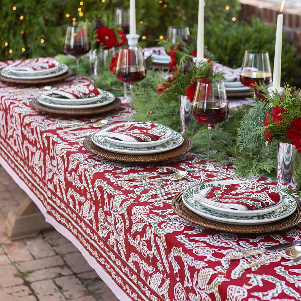 Decorative table setting with red and white patterned tablecloth, greenery, and wine glasses.