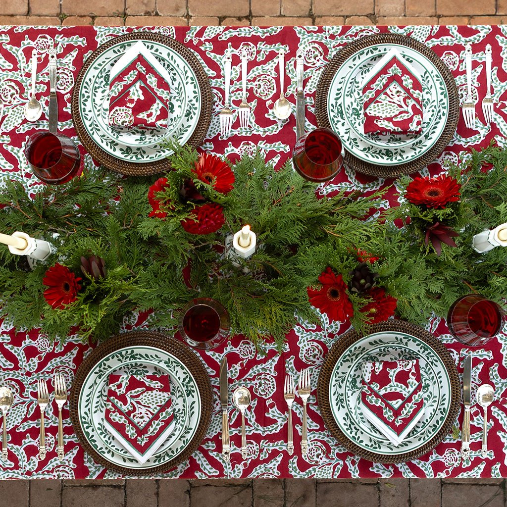 Decorative Christmas table setting with red and white patterned tablecloth, greenery, and festive plates.