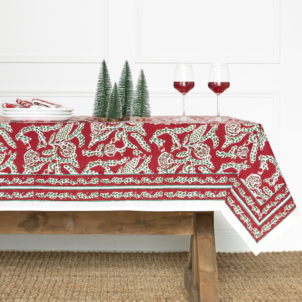 Tablecloth with reindeer design on a wooden table with wine glasses and Christmas trees.