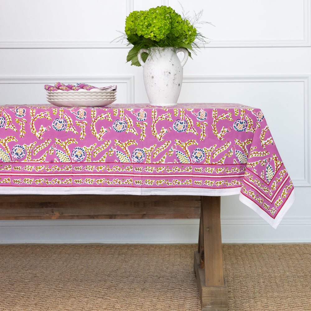 A dining table with the Climbing Dahlia Lilac Tablecloth featuring a floral design, placed against a white background