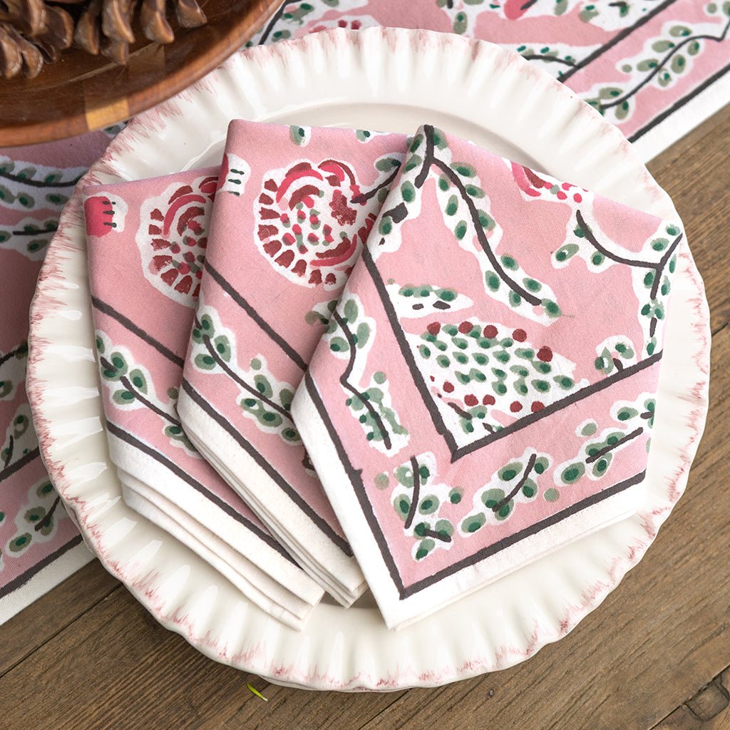 Pink patterned napkins on a white paper plate with a wooden surface and floral tablecloth in the background.