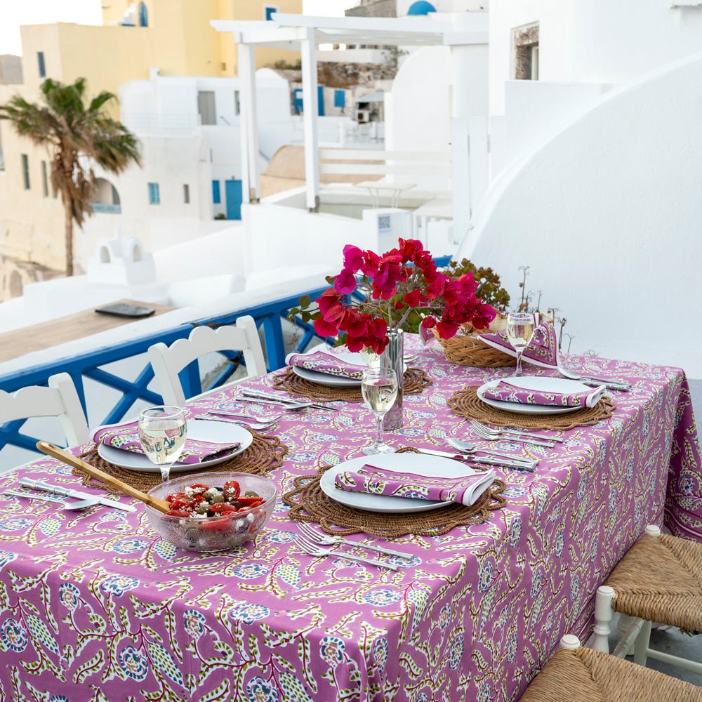 A set dining table with the Climbing Dahlia Lilac Tablecloth featuring a floral design, placed outdoors with a scenic background.