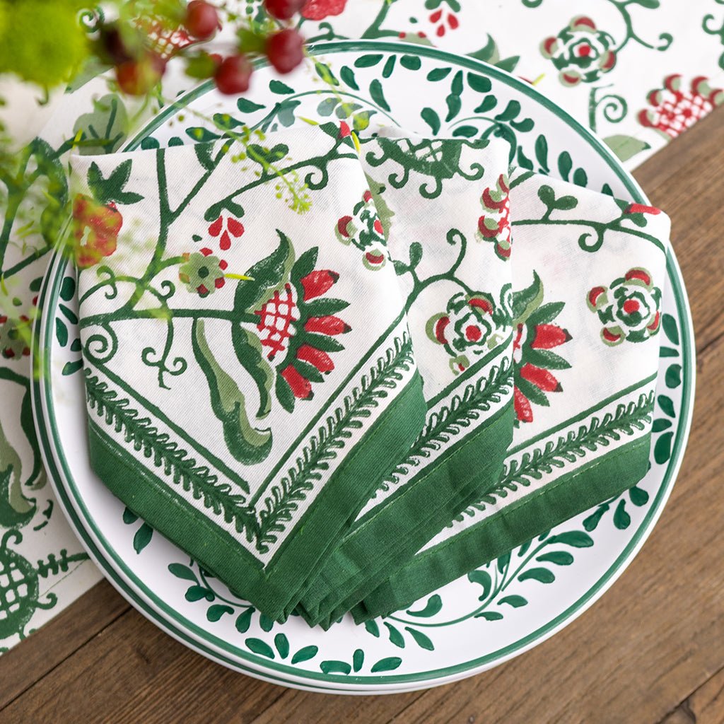 Decorative plate with green and red floral patterned napkins on a wooden surface