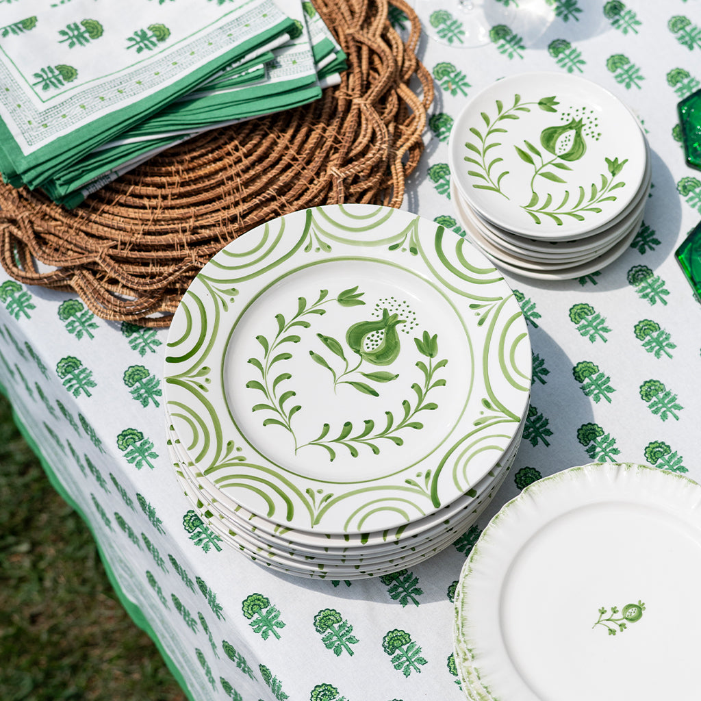 Stacks of white plates with green floral patterns on a tablecloth with similar design.