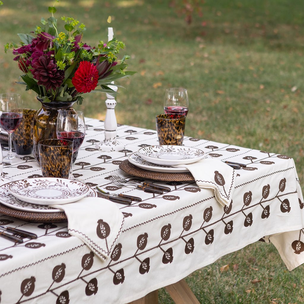 Dining table set with a floral centerpiece, glasses, and cutlery on a patterned tablecloth outdoors.