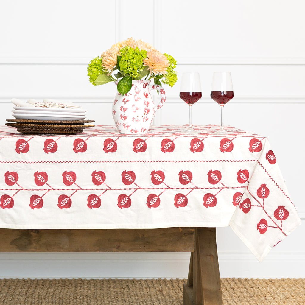 Table setting with a patterned tablecloth, flowers, and wine glasses on a wooden table.