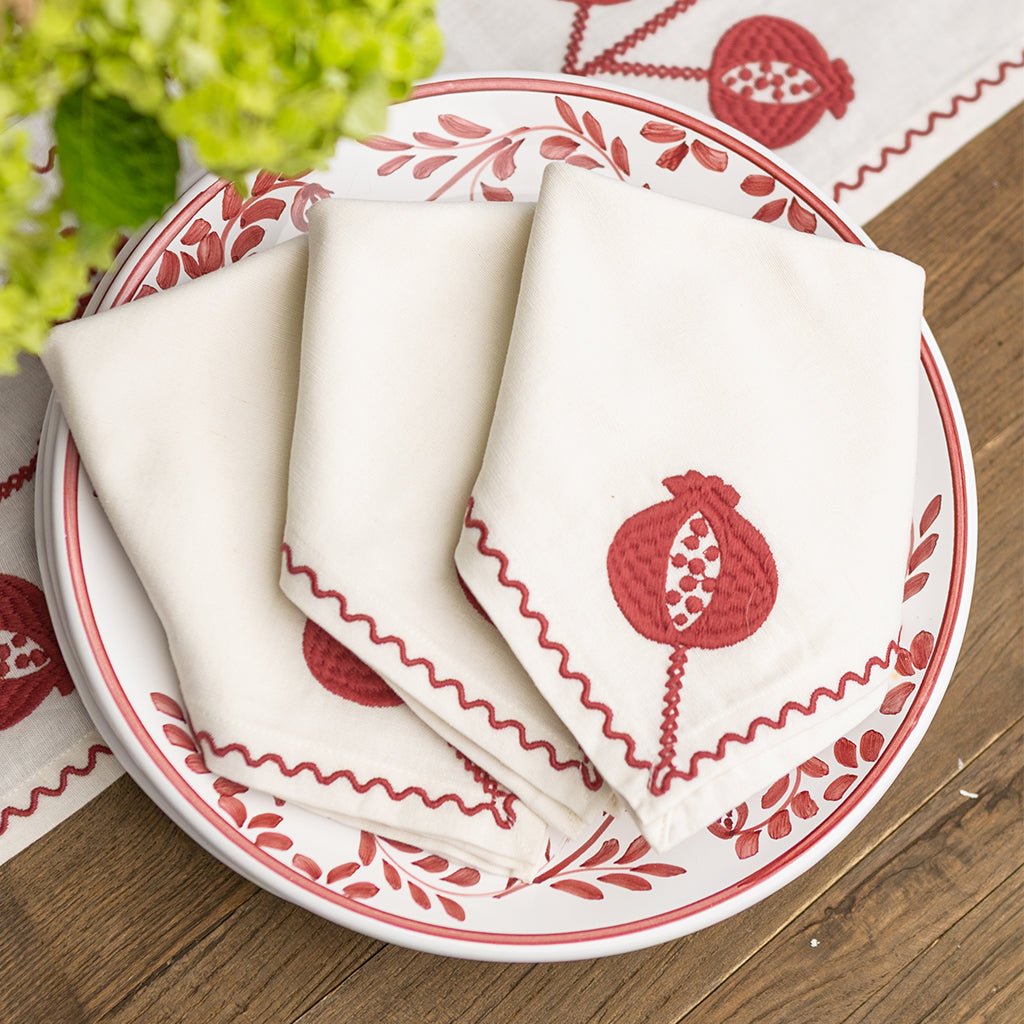 White napkins with red pomegranate design on a matching plate and placemat.