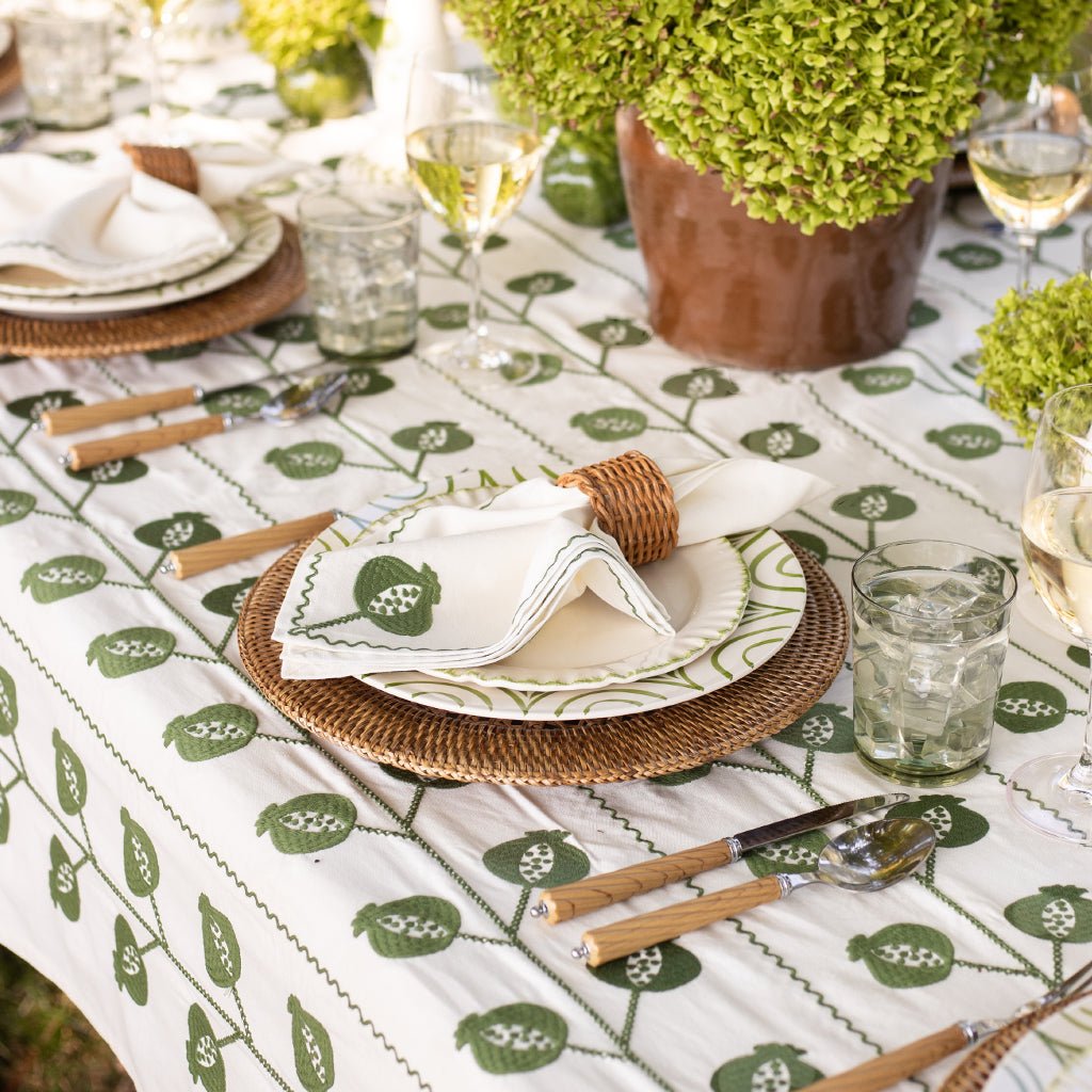 Dining table setting with green and white patterned tablecloth, wicker plates, and cutlery.