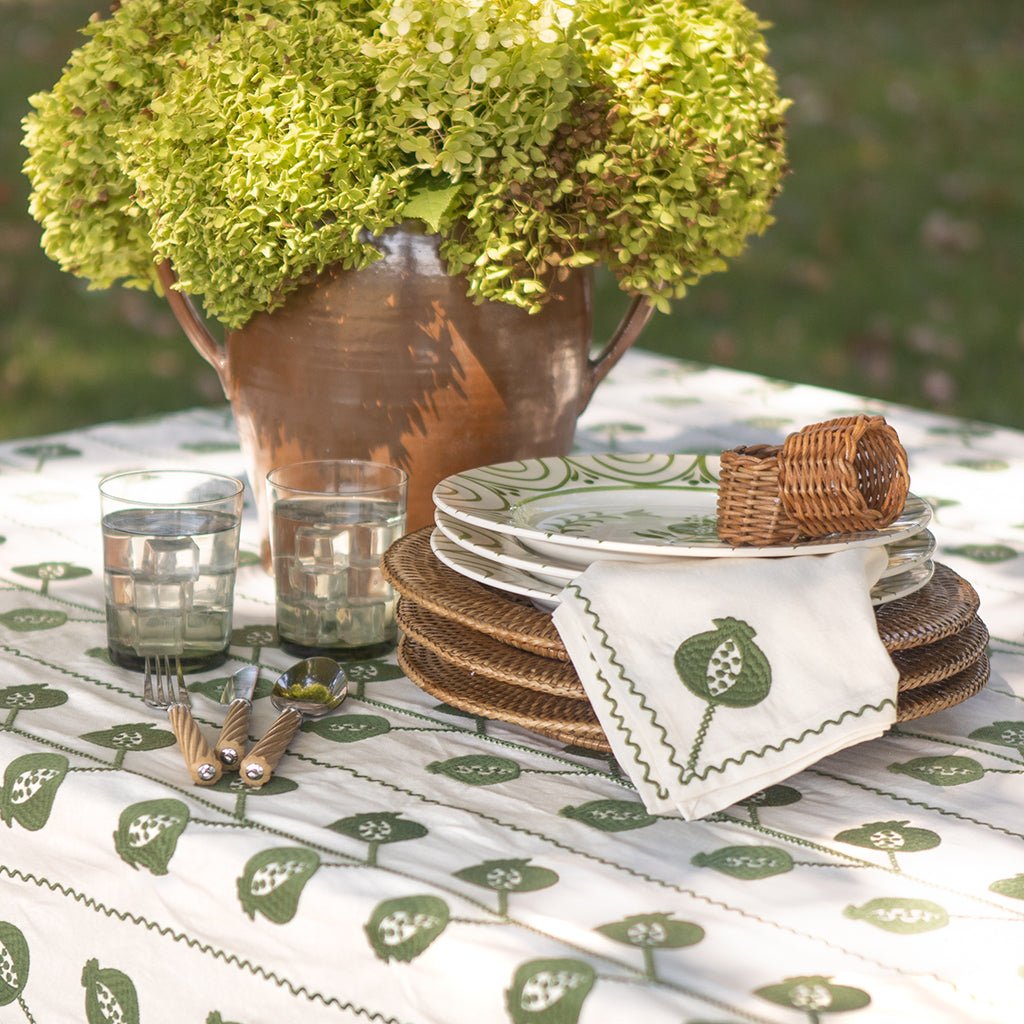 Outdoor table setting with floral arrangement, plates, glasses, and napkins on a patterned tablecloth.