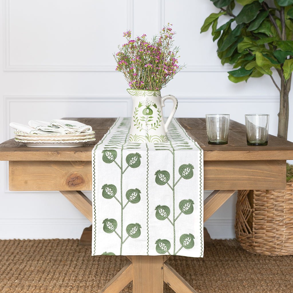 Table setting with a decorative table runner, pitcher, and glasses on a wooden table.