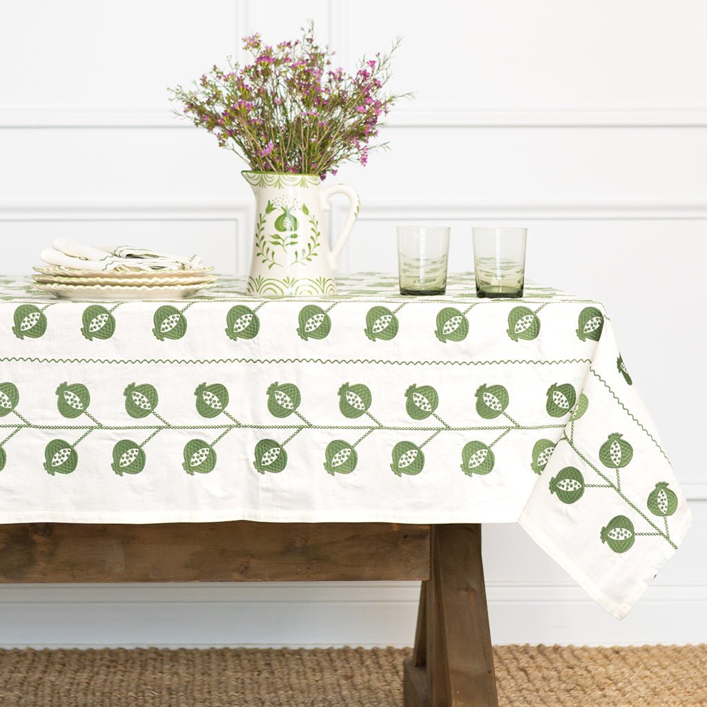 Tablecloth with green leaf pattern on a wooden table with a vase of flowers and glasses.