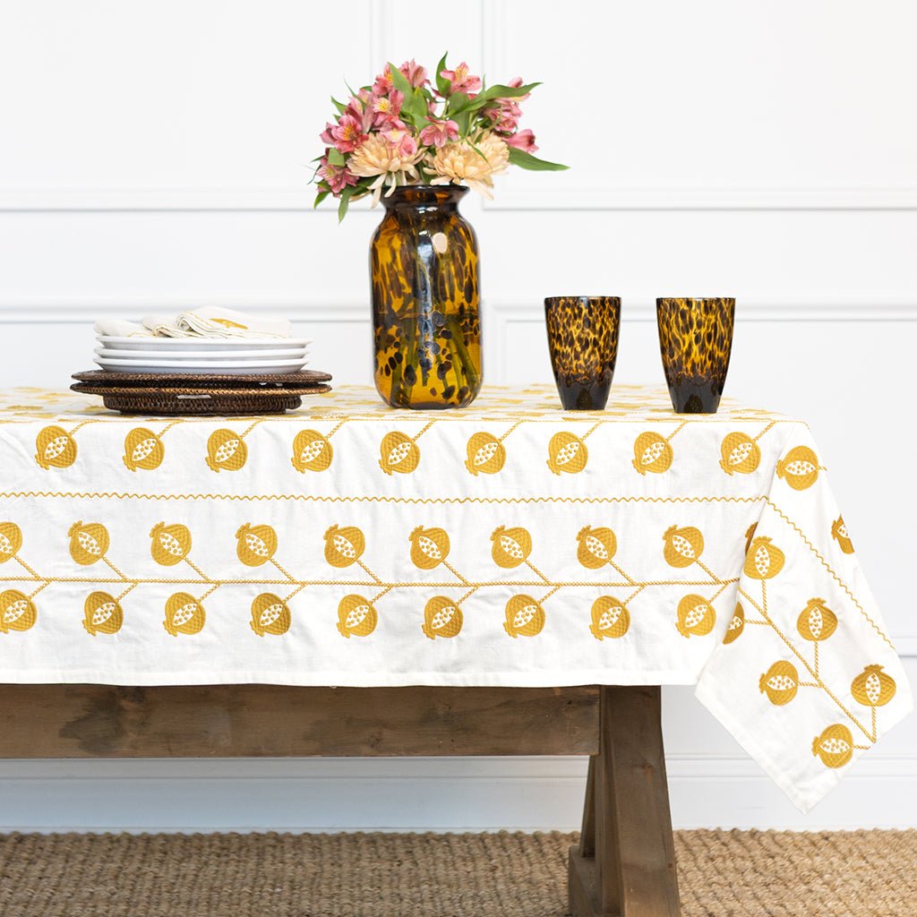 Table setting with a white tablecloth featuring yellow floral patterns, a vase with flowers, and leopard print glasses.