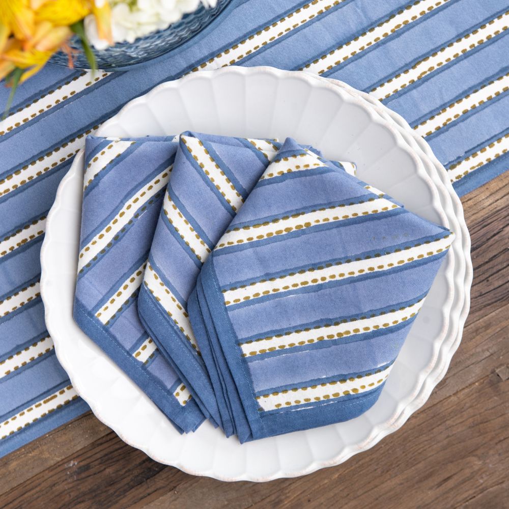 Blue striped napkins on a white plate with a striped tablecloth in the background