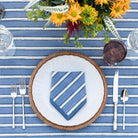 Table setting with blue and white striped napkin, white plate, silverware, and floral arrangement on a blue and white striped tablecloth.