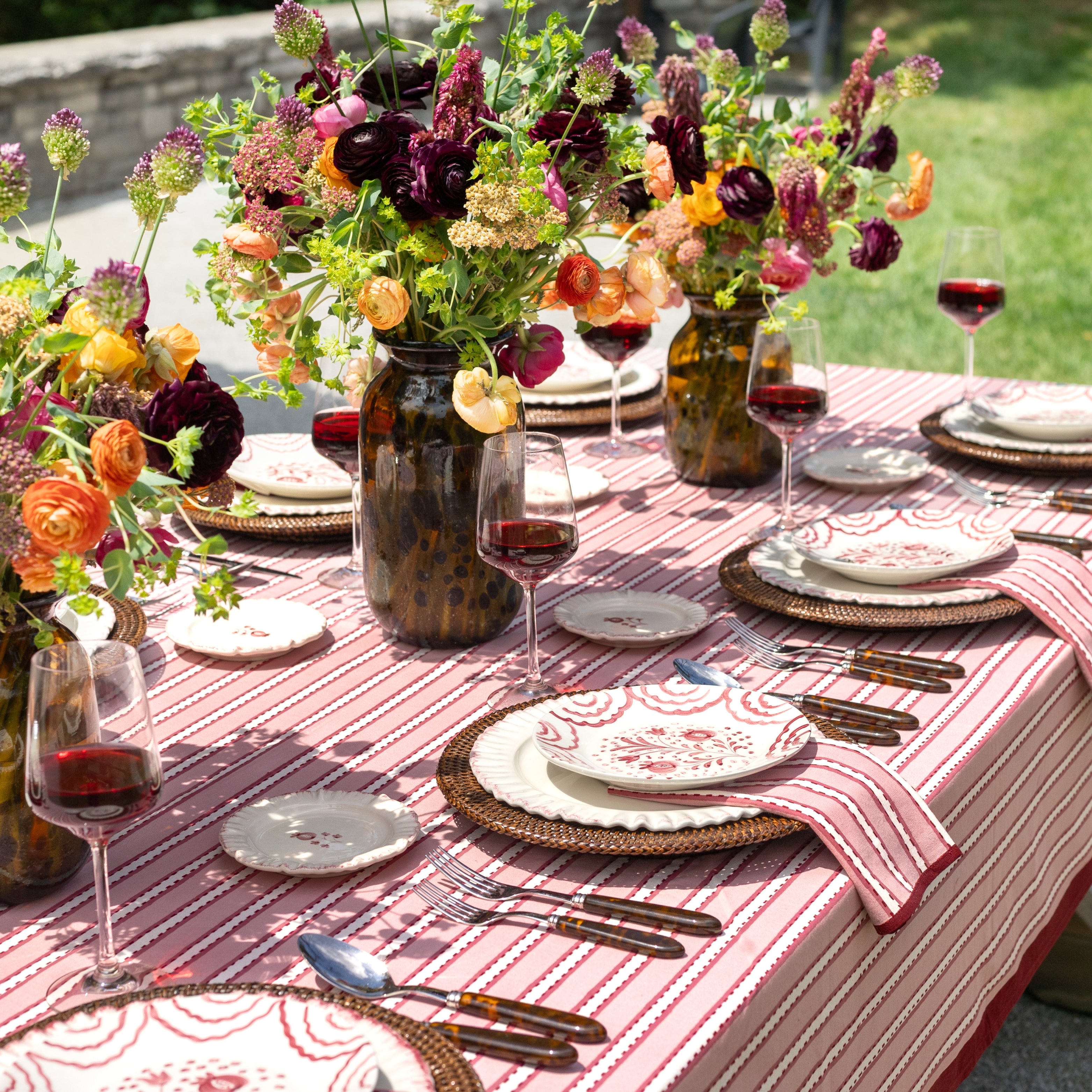 Elegant outdoor dining table setting with floral arrangements, red wine, and striped tablecloth.