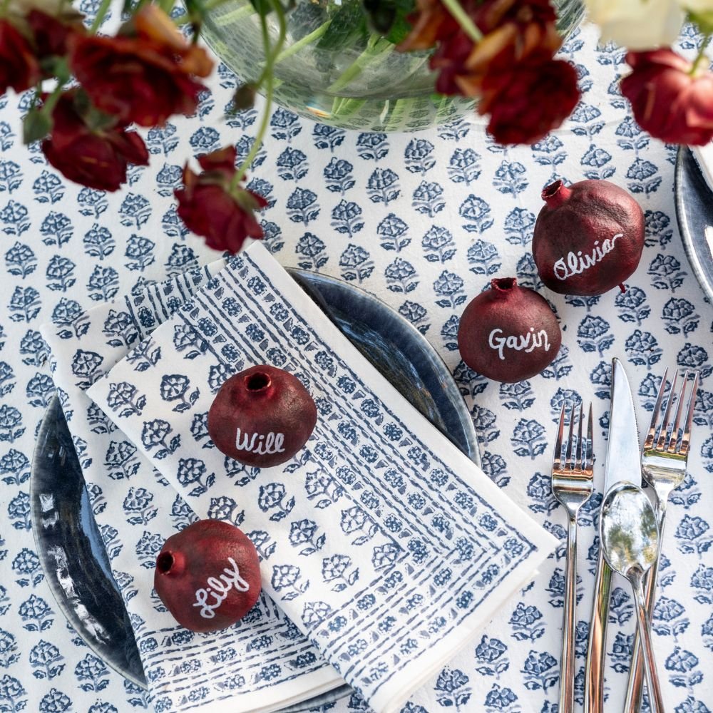 Table setting with personalized red pomegramates on a blue and white patterned tablecloth.