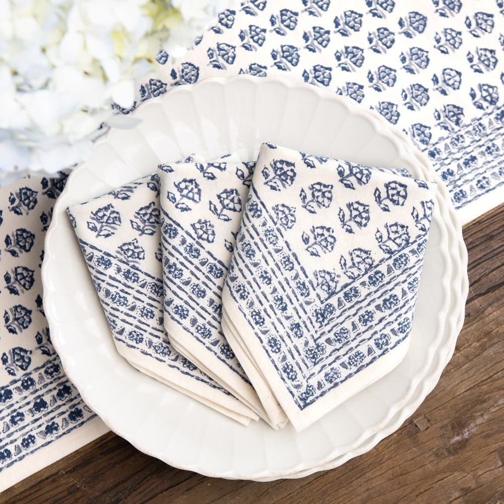 Set of blue and white patterned napkins on a white plate with a floral tablecloth in the background.