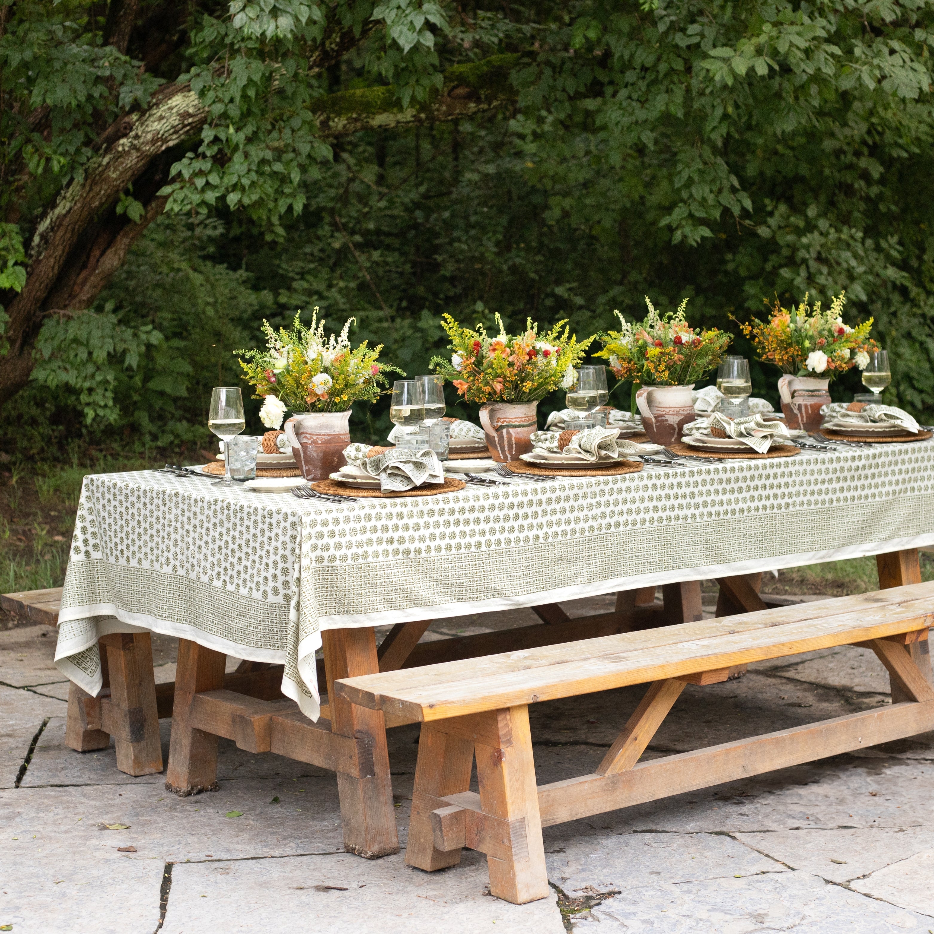 Outdoor table setting with floral centerpieces and tablecloth in a garden.
