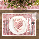 Table setting with white plate, cutlery, and floral arrangement on a patterned placemat.