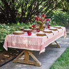 Dining table set for a meal outdoors with a red and white patterned tablecloth.