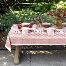 Dining table set on a red and white patterned tablecloth set in a garden.