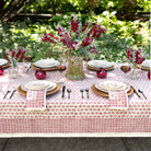 Elegant outdoor table setting with floral centerpieces and red patterned tablecloth.