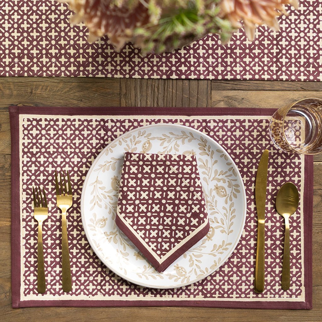Dining table setting with a patterned placemat, plate, and cutlery on a wooden surface.