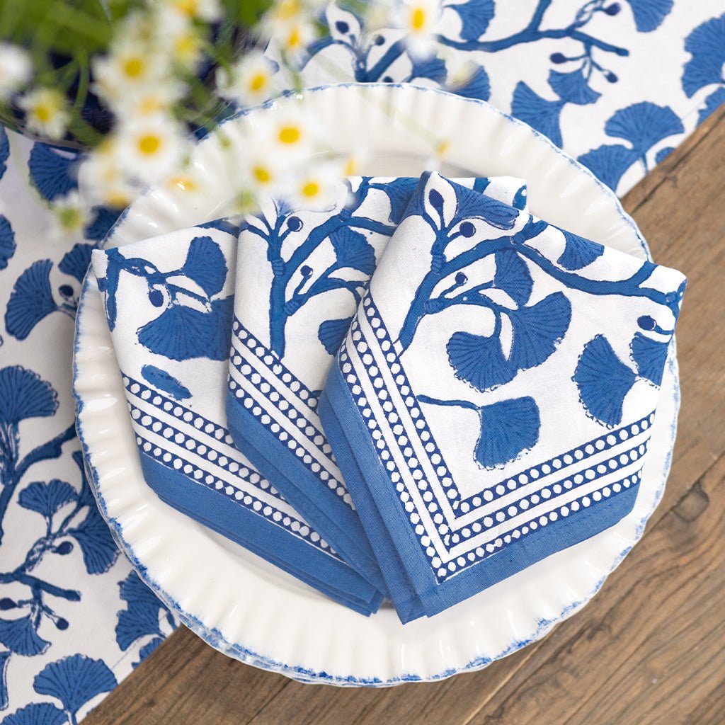 Set of blue and white patterned napkins on a wooden table with floral elements.