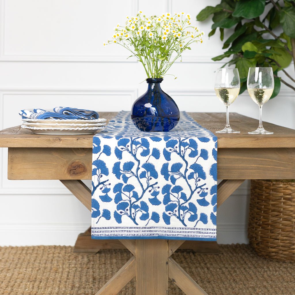 Table setting with a blue floral table runner, vase with flowers, and wine glasses.